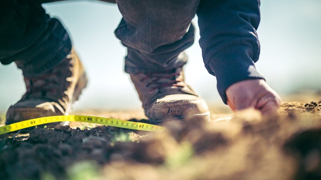 pexels-photo-7763709 Focused shot of a person in boots measuring soil with tape outdoors.